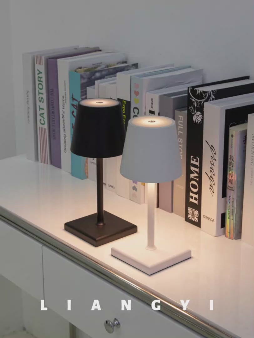Sigtuna Mini opladelige bordlamper i sort og hvid placeret foran bøger på moderne reol