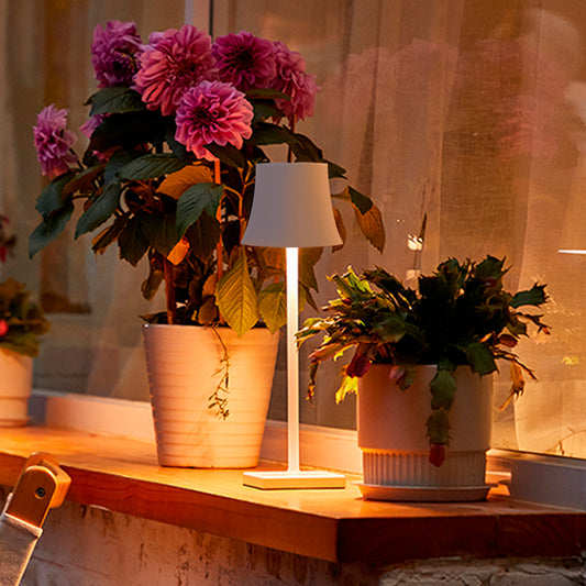 Sigtuna opladelig bordlampe i hvid med varmt lys på terrassebord ved blomster om aftenen
